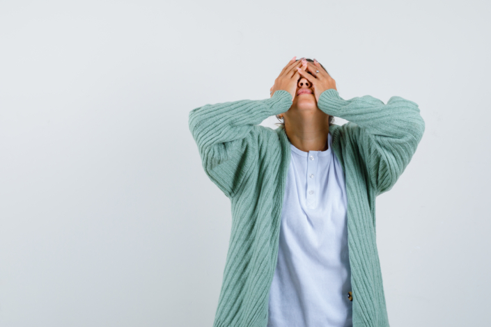 young lady covering face with hands in t-shirt, jacket and looking tired , front view.