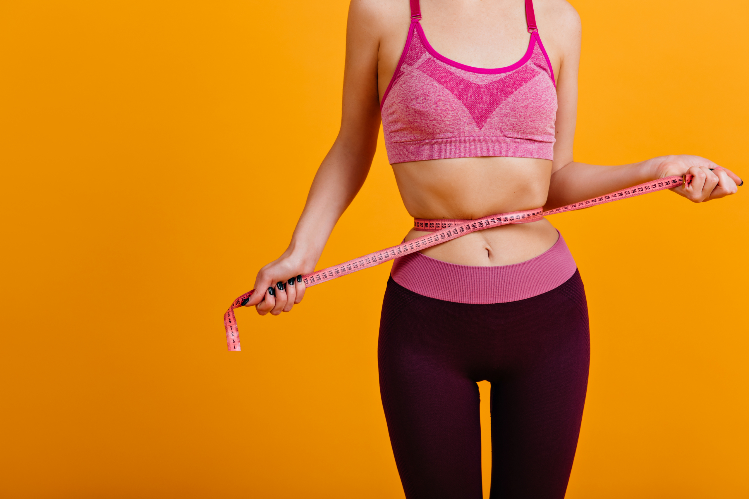 Indoor shot of woman in good shape after diet. Shapely fitness girl using measure tape